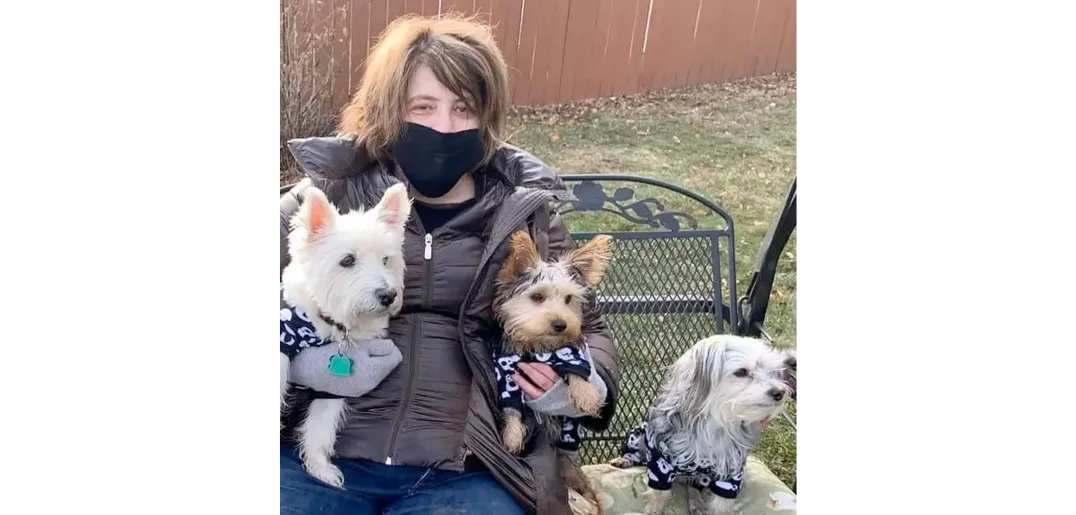 Bridget sitting on a bench with her three dogs, wearing a face mask