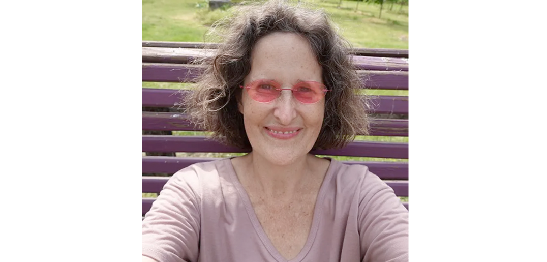 A headshot of Peace, wearing pink sunglasses and smiling.