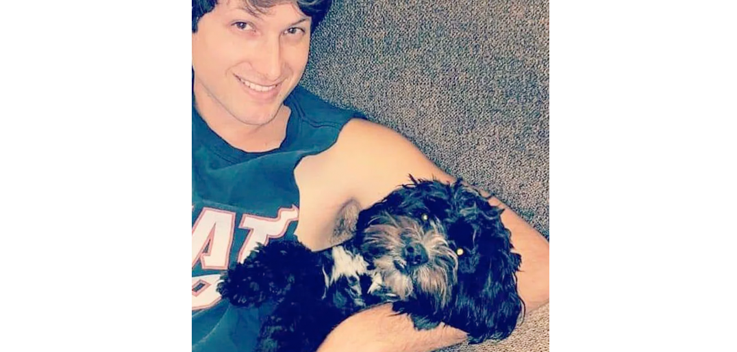 Travis lying down with his dog, both of them smiling.
