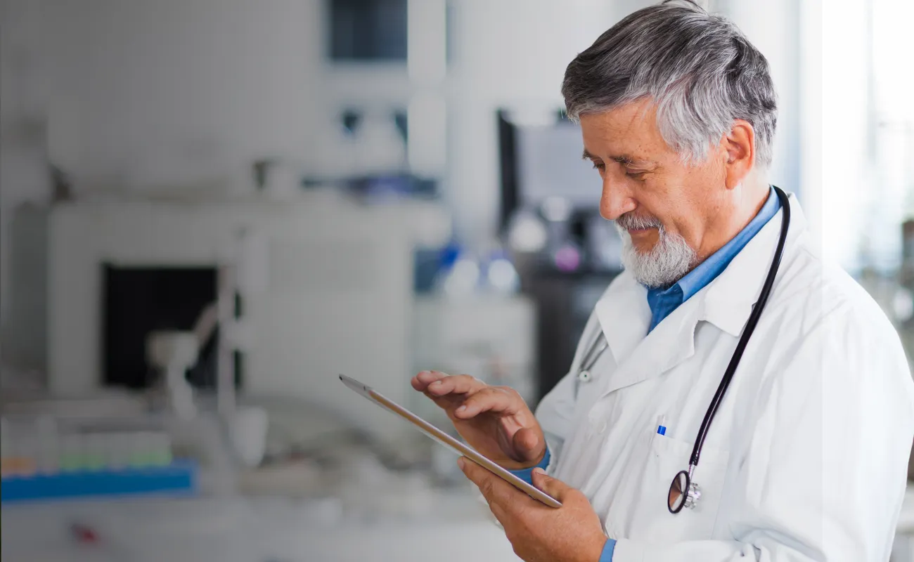 A doctor is in his office, working on his tablet.