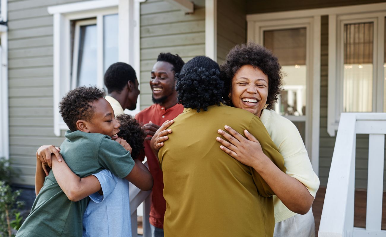 A family is greeting guests outside their home, hugging them and smiling