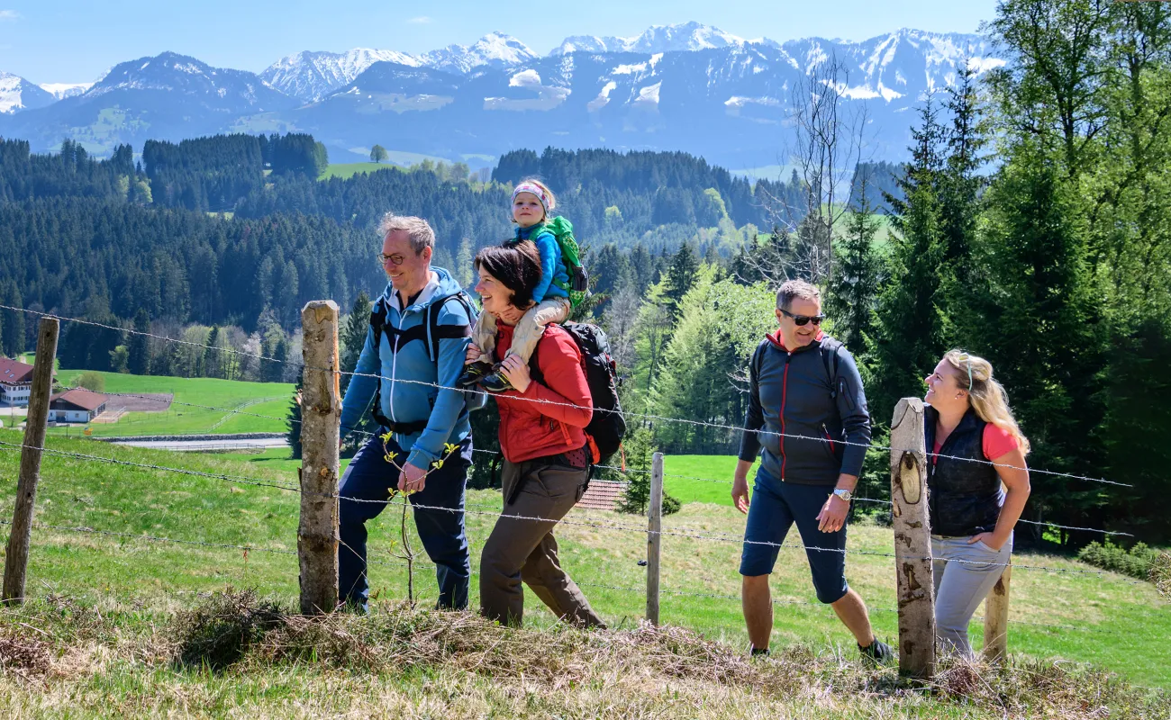 A family is going on a hike with mountains in the background, and everyone is smiling.