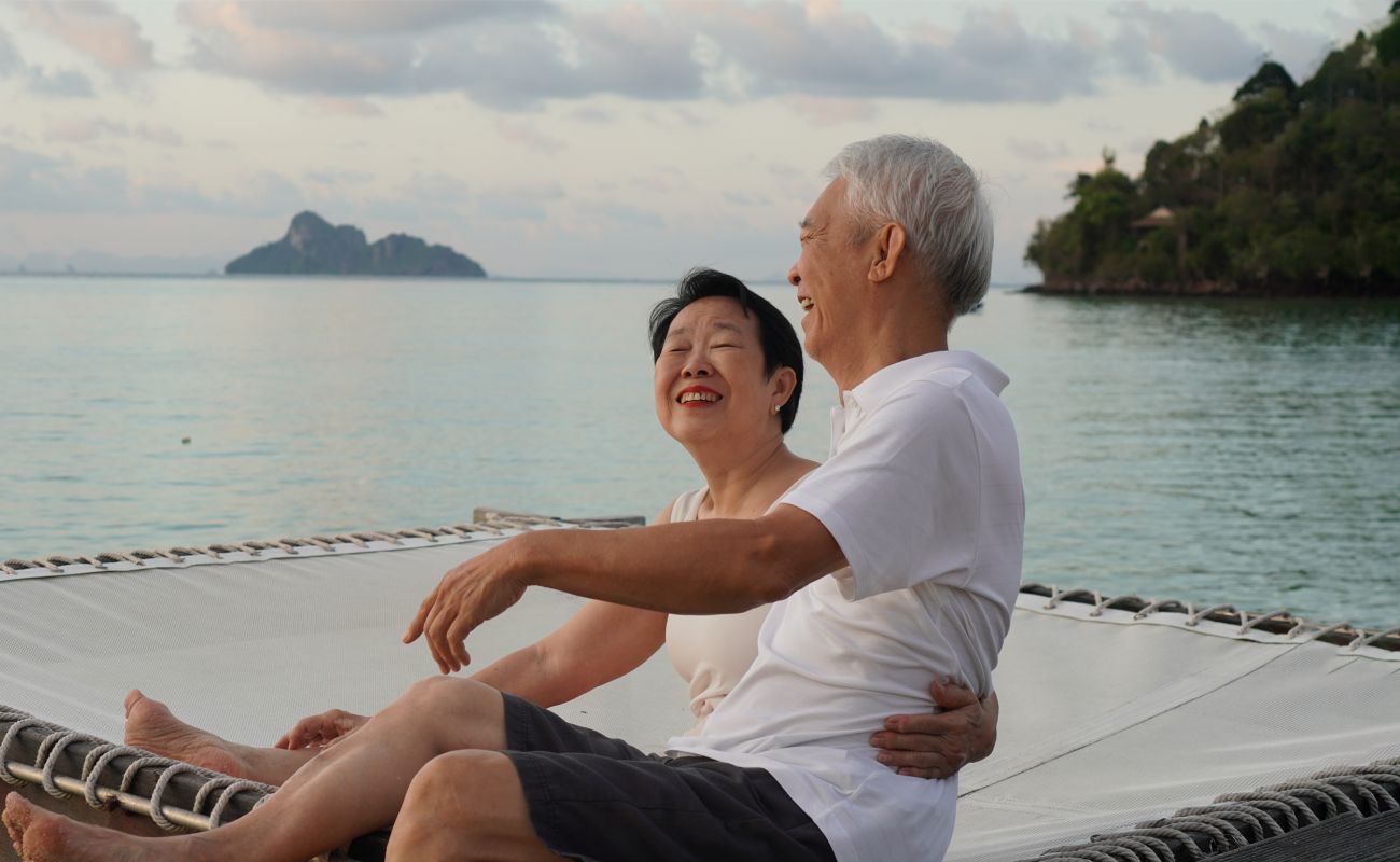 A woman and a man are side-hugging and laughing while sitting in front of water