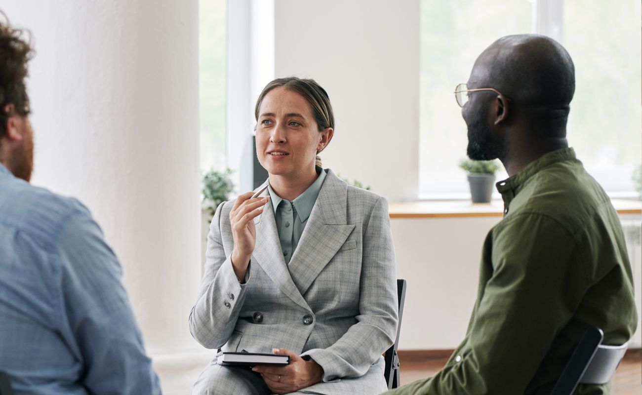 A woman, wearing a plaid suit, having a discussion with a small group of people. 