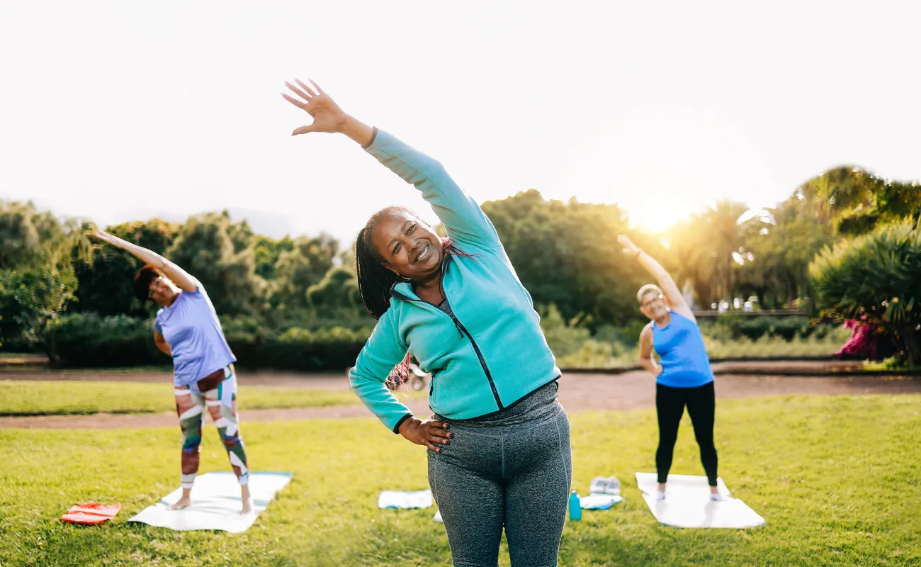 A small group of women standing on the grass, stretching and preparing for yoga.