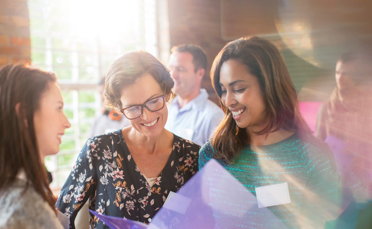Three women are looking down at a folder while smiling and discussing with one another