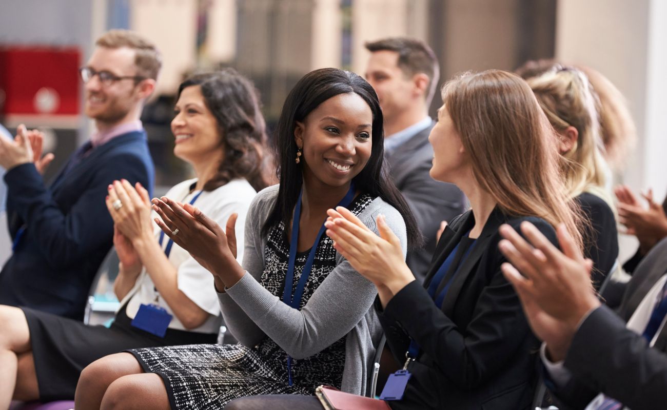Two women sitting in an audience while applauding at a conference