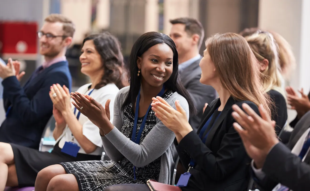 Two women sitting in an audience while applauding at a conference