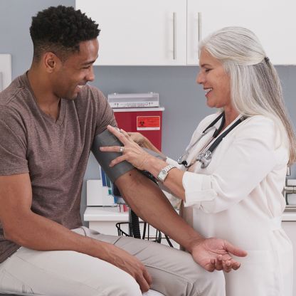 A man is getting his blood pressure checked by a doctor, and both of them are smiling.
