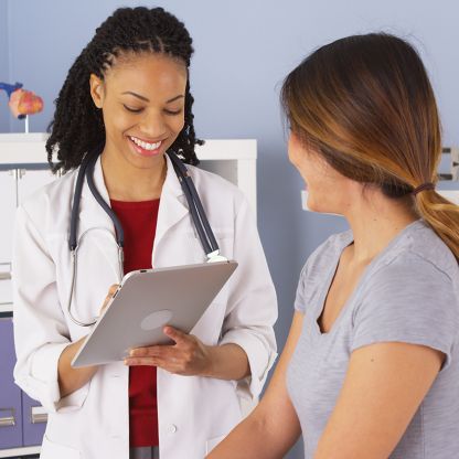 A doctor is actively writing information down on her clipboard while smiling with her patient.