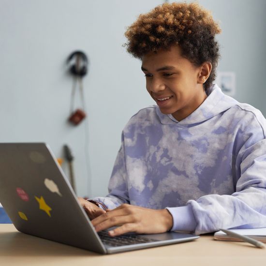 A young adult is working on his laptop and smiling.