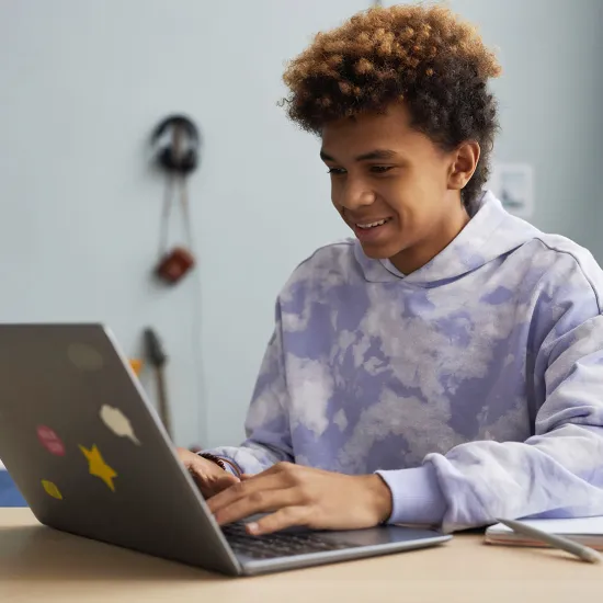 A young adult is working on his laptop and smiling.