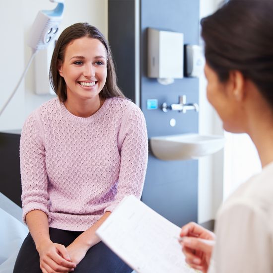 An image of a woman sitting on an exam table, smiling at her doctor.