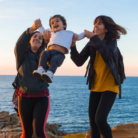 Two women are swinging a toddler, and all three of them are smiling.