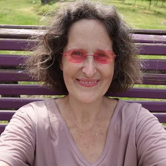 A headshot of Peace, wearing pink sunglasses and smiling.