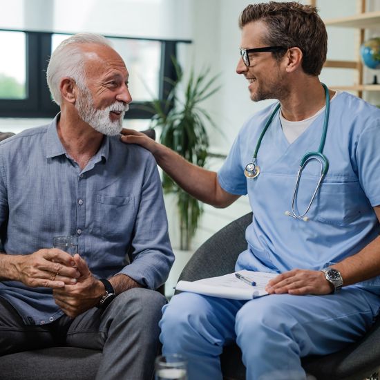 A man and his doctor are actively discussing and smiling while the doctor holds a clipboard.